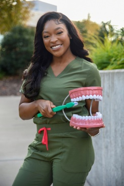 Student dentist, Taylor Jackson, holding large model teeth and a toothbrush